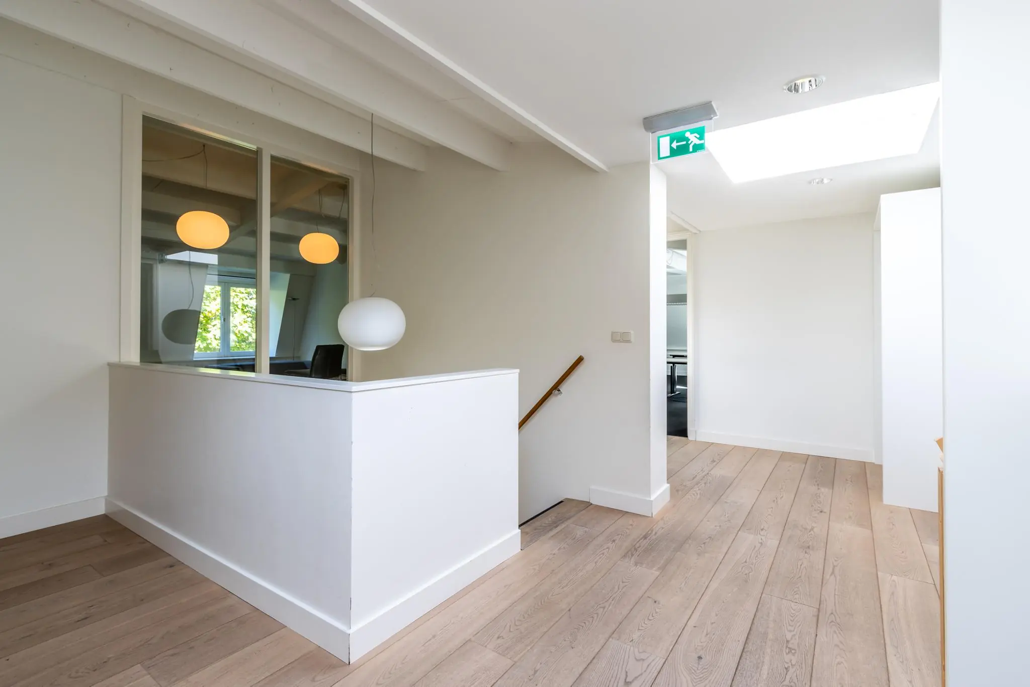 Lichte bovenverdieping van een modern kantoor aan de Langbroekerdijk met houten vloer, wit interieur en zicht op een trapgat.